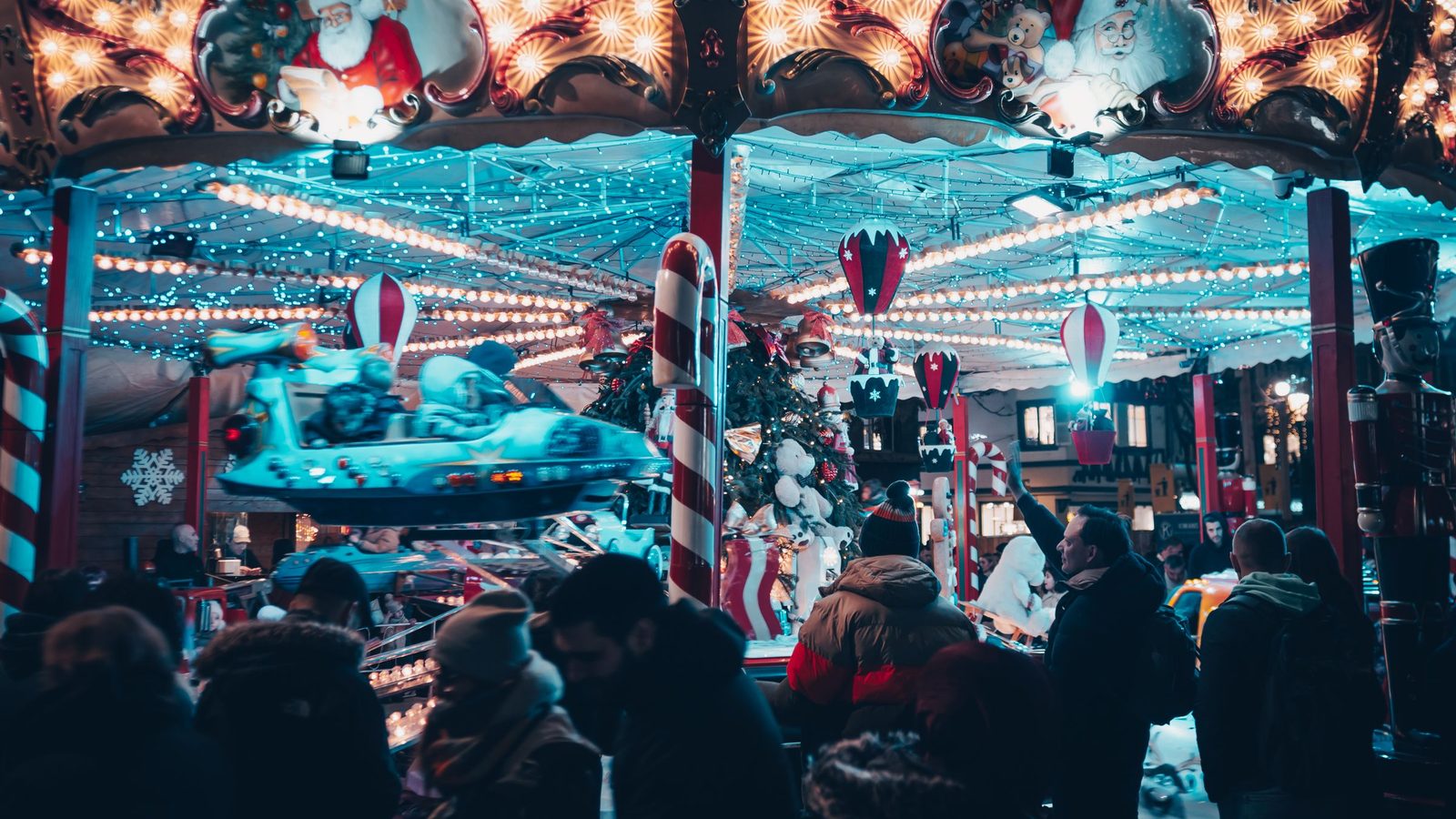 Verlichte draaimolen op een kerstmarkt bij avond, met bezoekers op de voorgrond