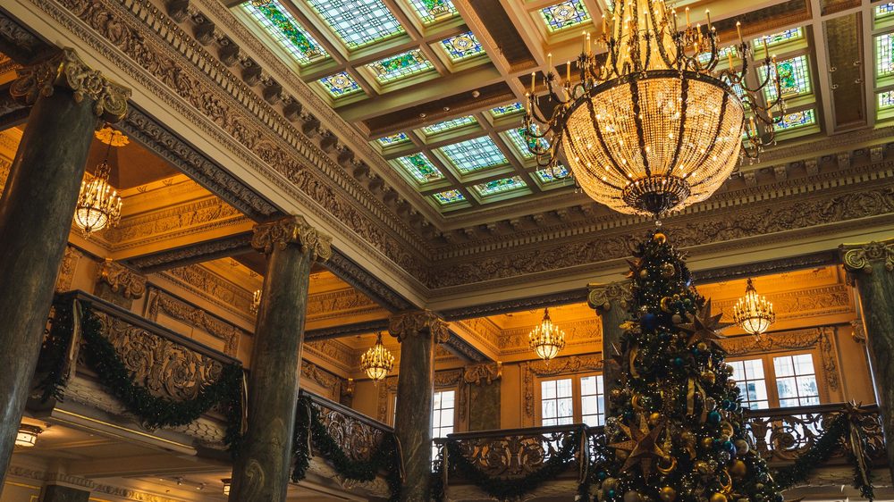 Versierde kerstboom onder een grote kroonluchter in een rijk versierde historische zaal