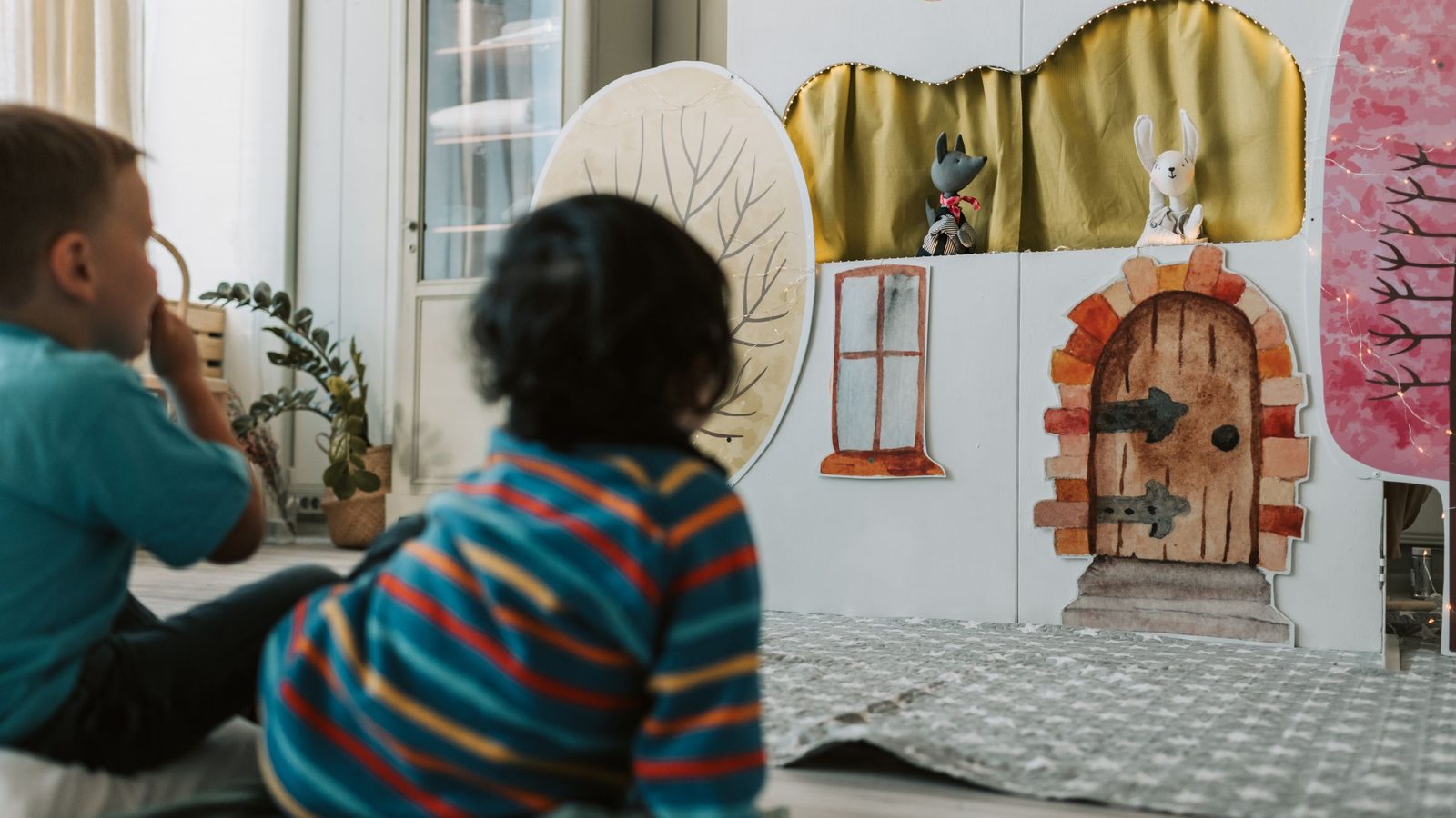 Twee kleine kinderen zitten op de grond en kijken naar een poppenkast met een geschilderd huisje