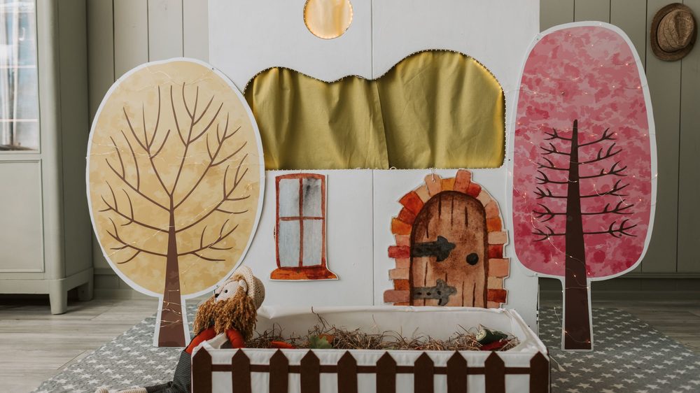 Zelfgemaakt poppentheater met een houten deurtje, geschilderde bomen en een pop achter een hekje