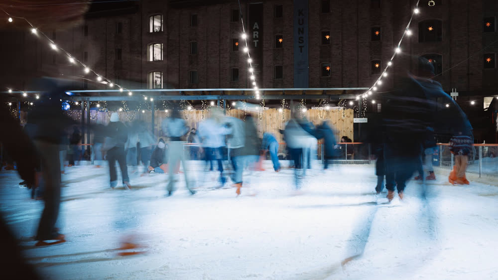 Schaatsers op een buitenijsbaan 's avonds onder lichtslingers