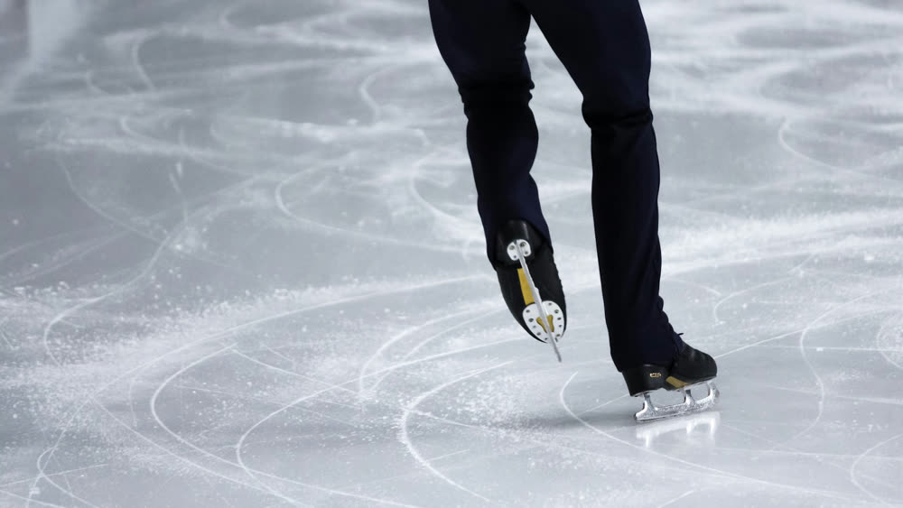 Benen van een schaatser op ijs vol krassen van schaatsijzers