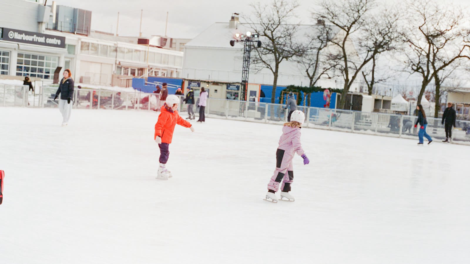 Twee kinderen met een helm en winterjas schaatsen op een buitenijsbaan